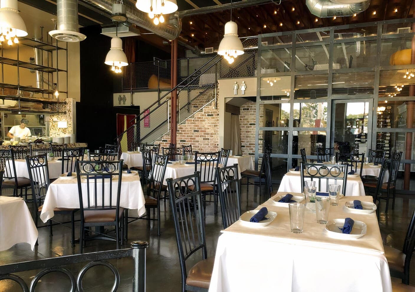 The Monzú dining room set for service — white tablecloths, exposed brick, glass wine room