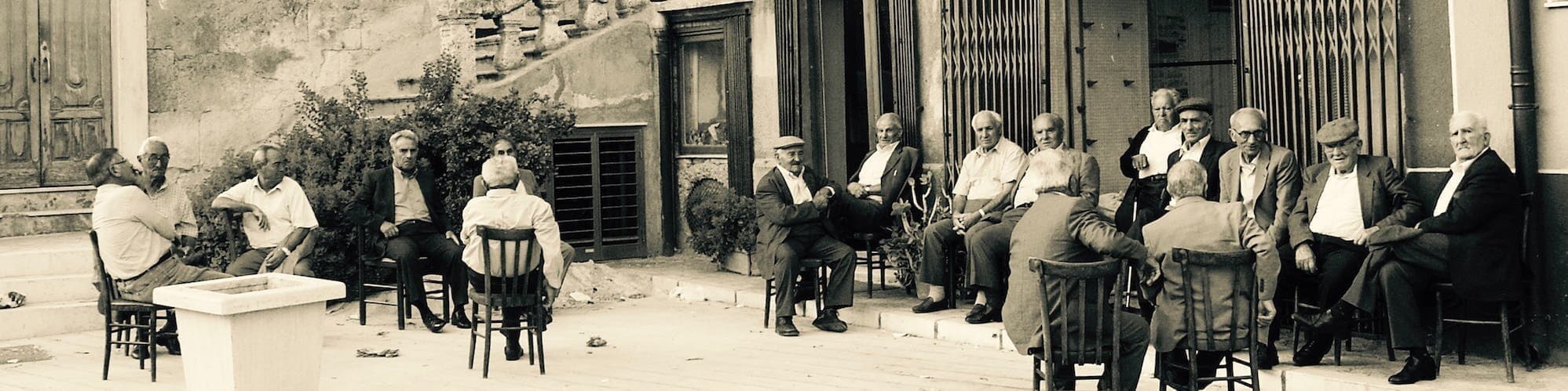 Old friends gathered on chairs outside a café in Sicily